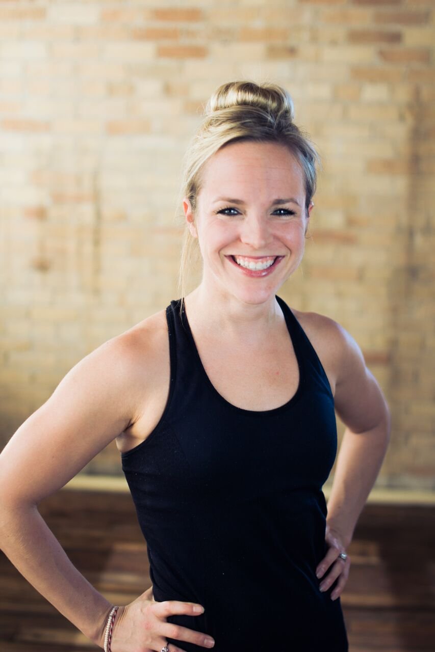 Katie Schutte smiling, hands on hips, in front of a brick wall